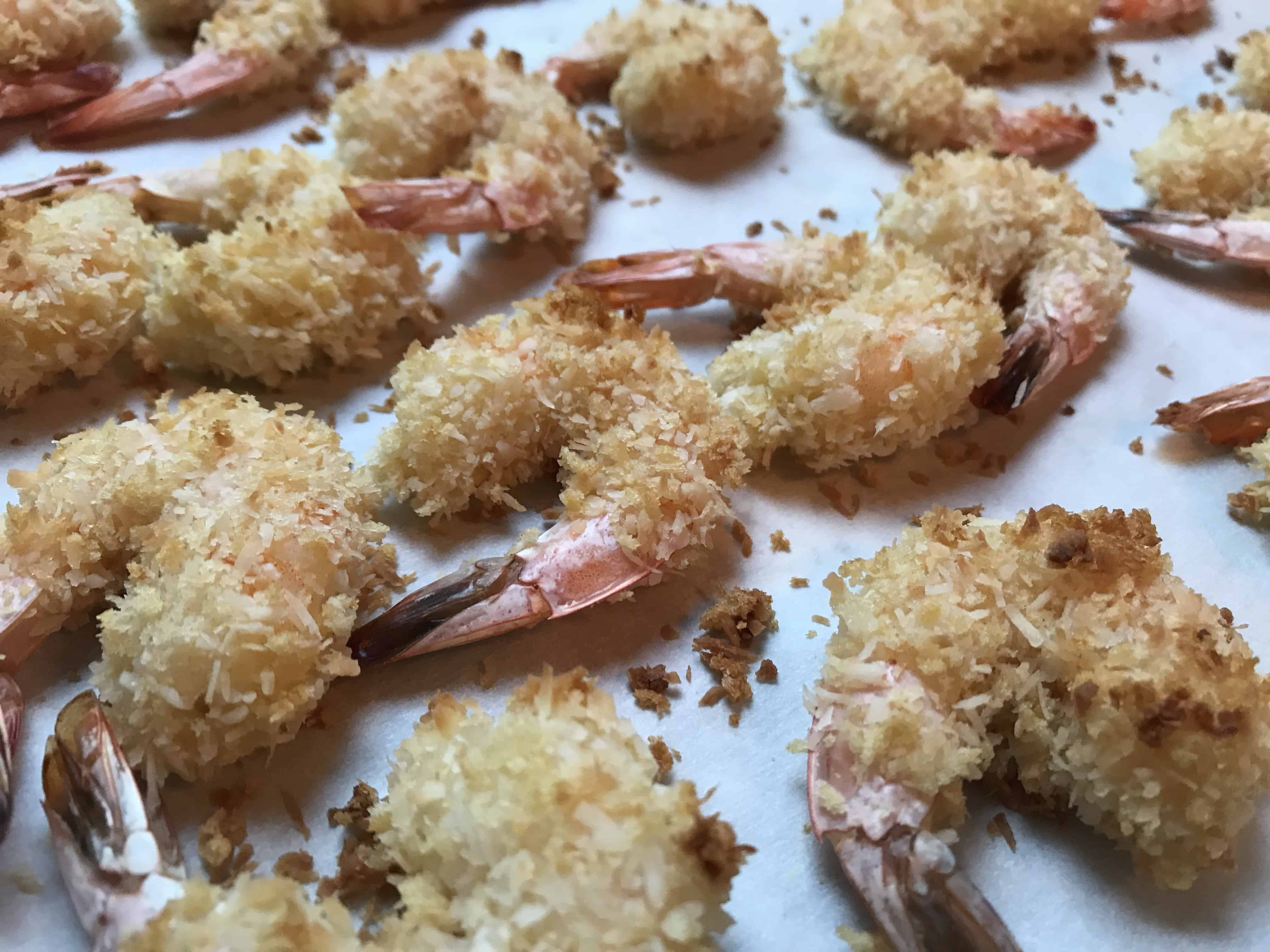 side shot of baked coconut shrimp on parchment paper. 