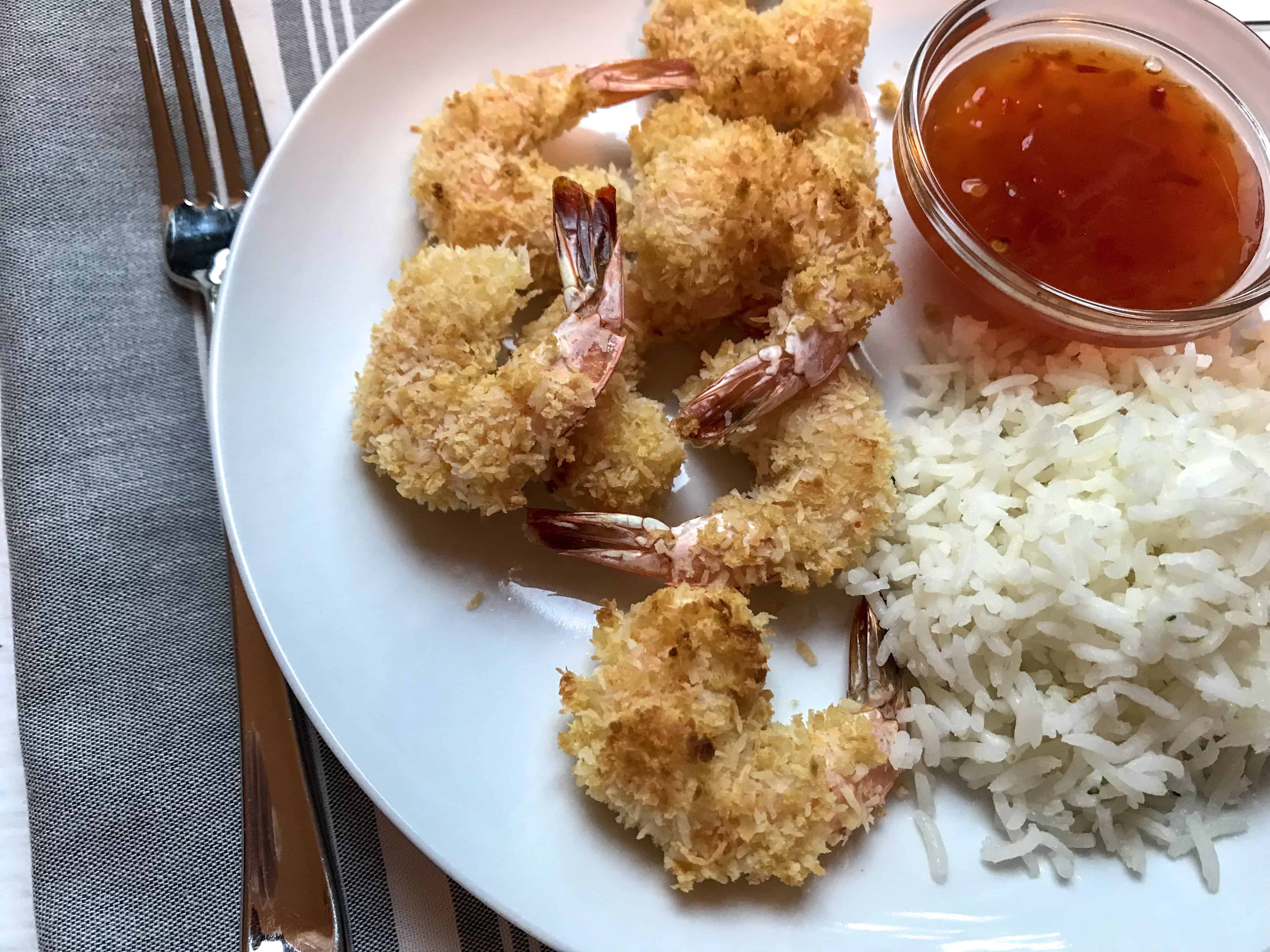 plate of baked coconut shrimp on white plate with rice and small bowl of Thai chili sauce.