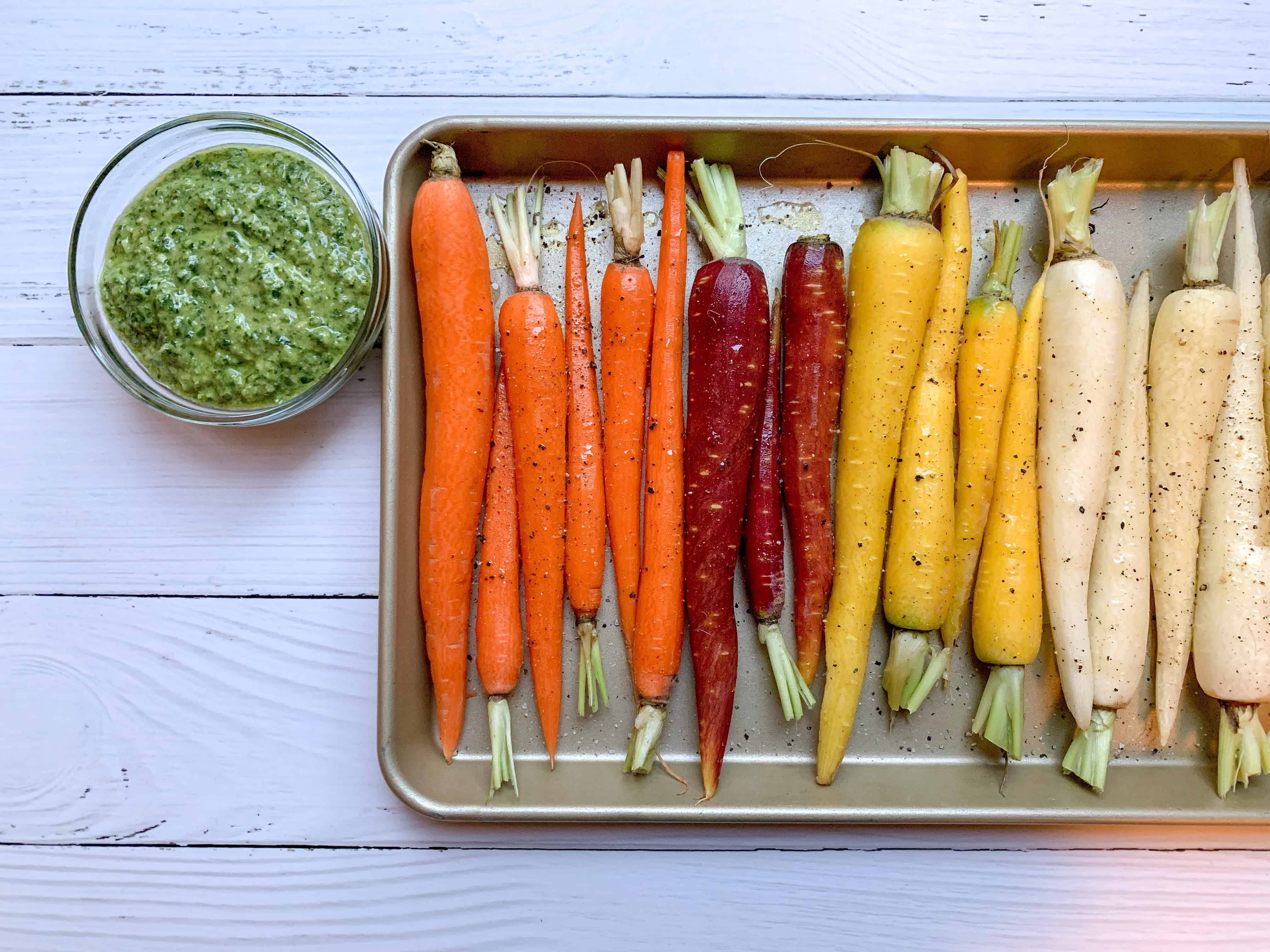 baking sheet with rainbow carrots and bowl of carrot top pesto