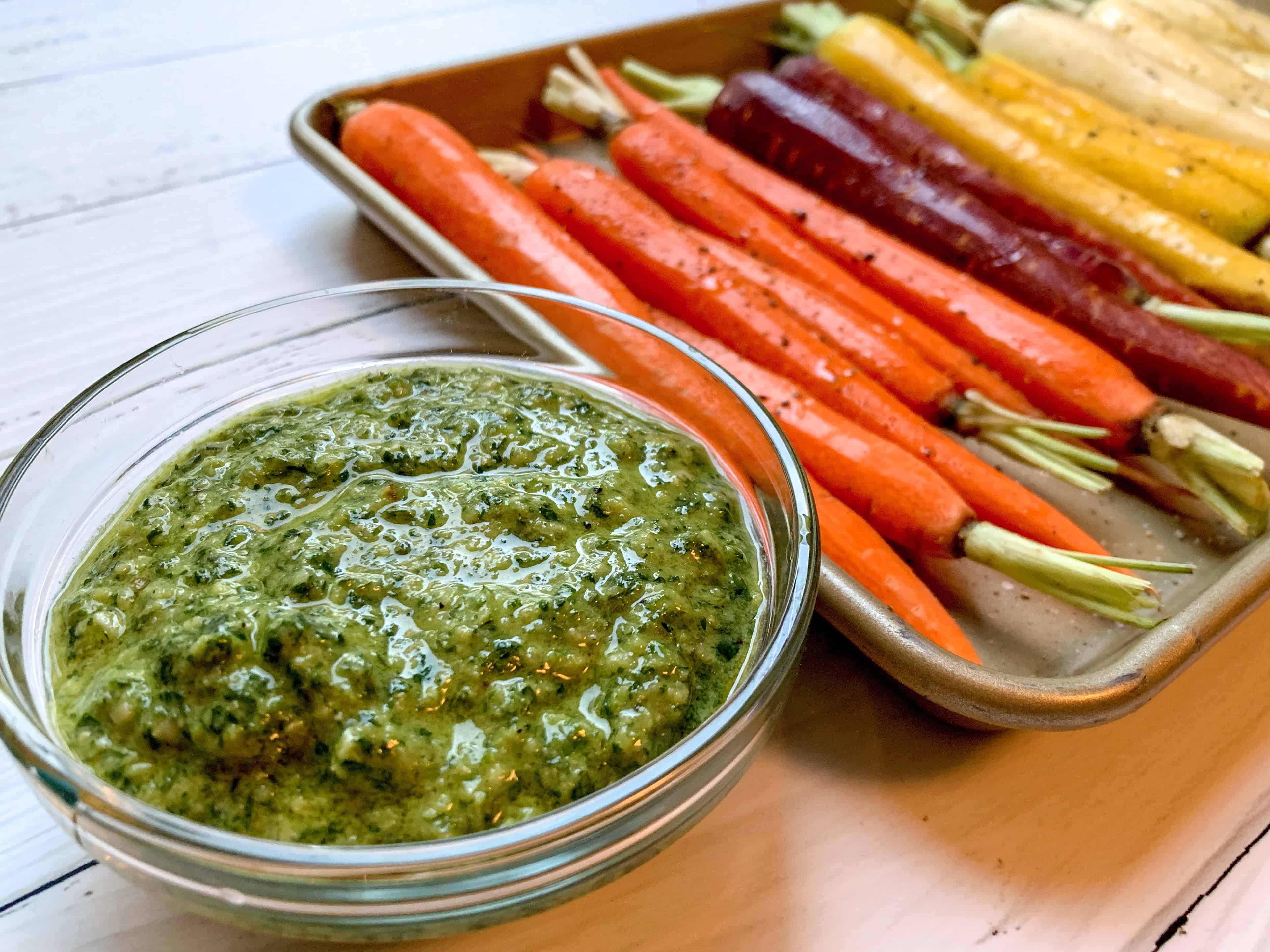 rainbow carrots on baking sheet with bowl of pesto next to sheet. 