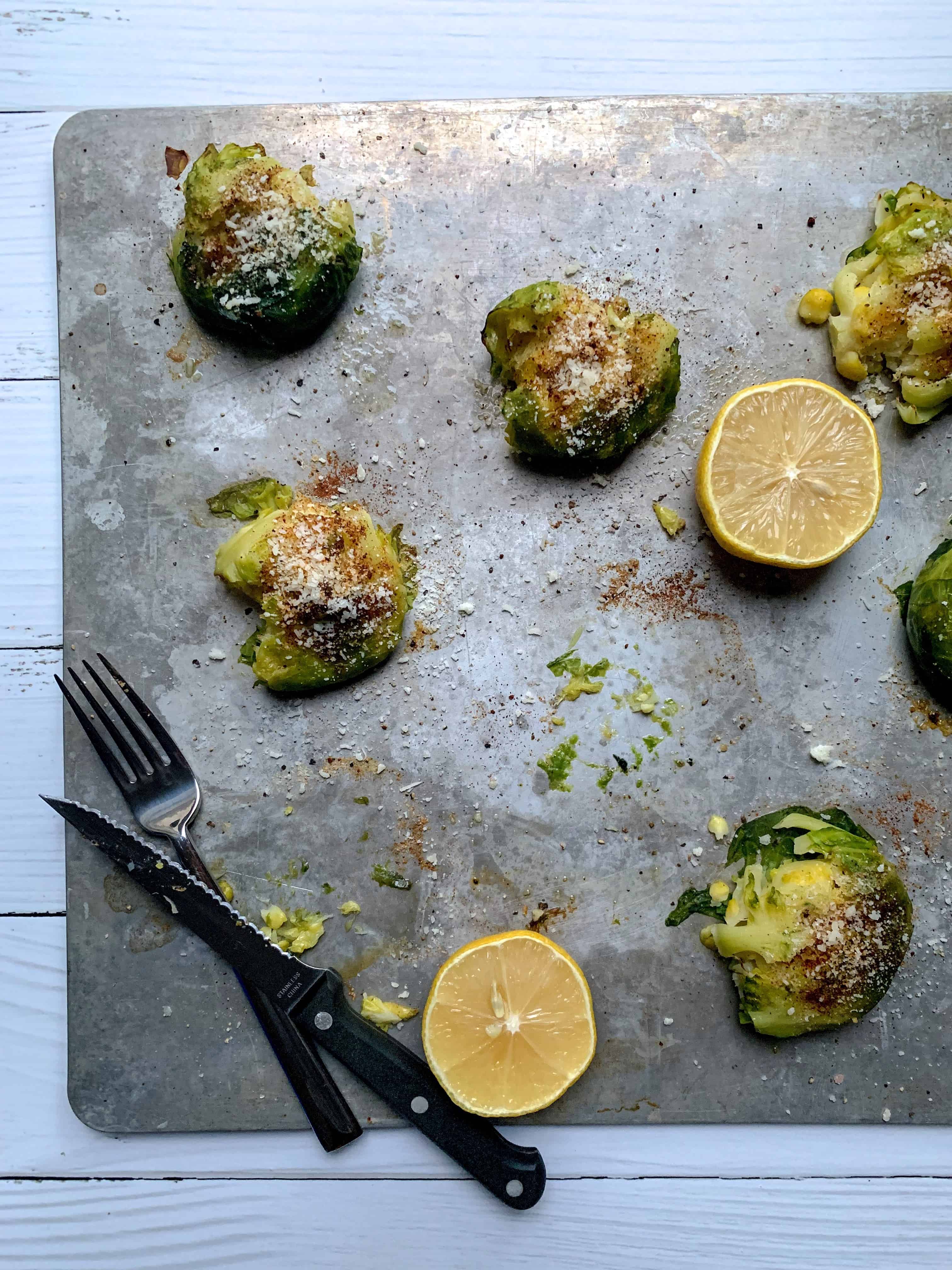 aerial shot of roasted brussels on sheet pan with lemon halves and fork and knife. 
