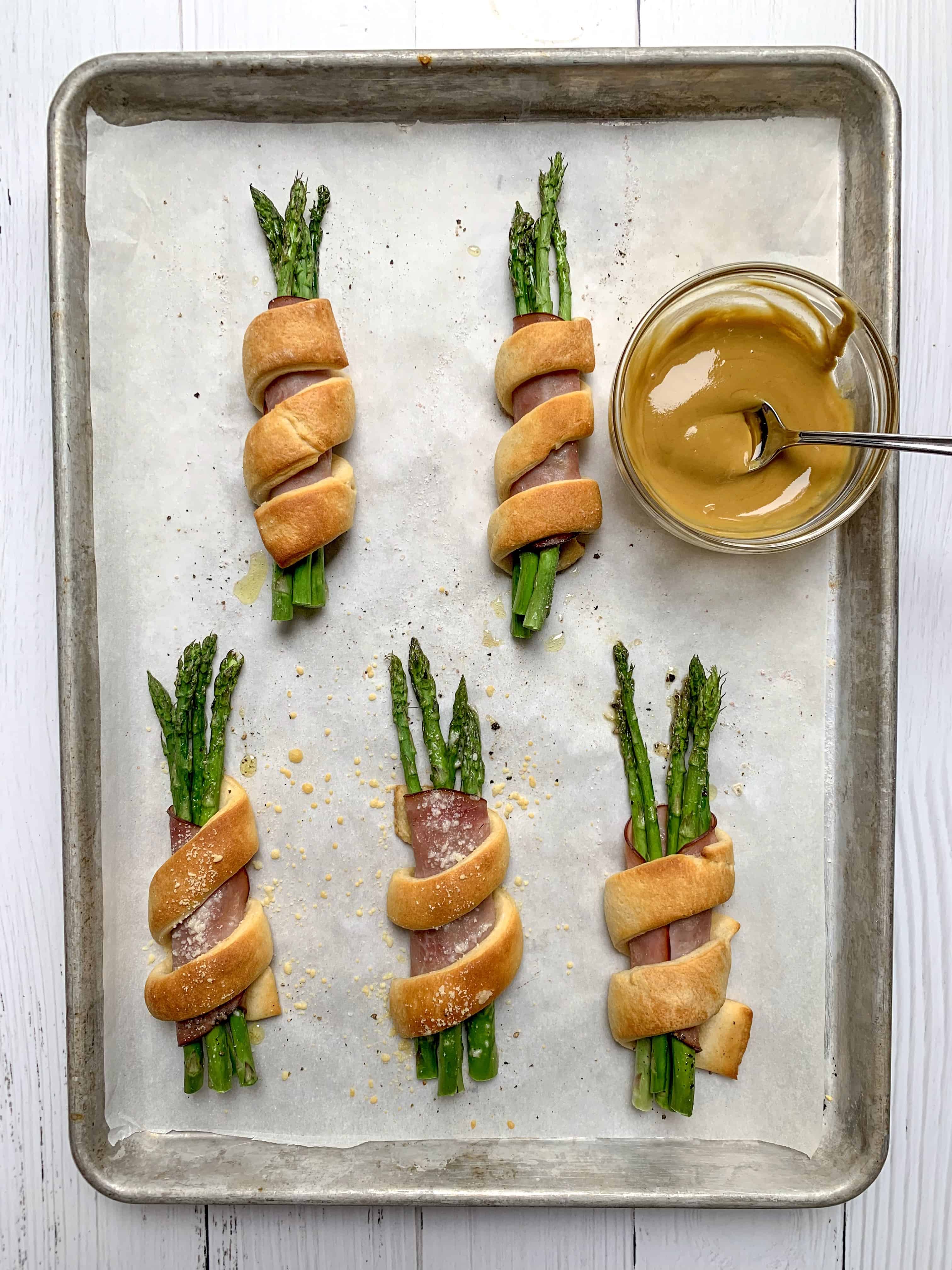 aerial view of 5 wrapped asparagus and ham bundles with bowl of honey mustard