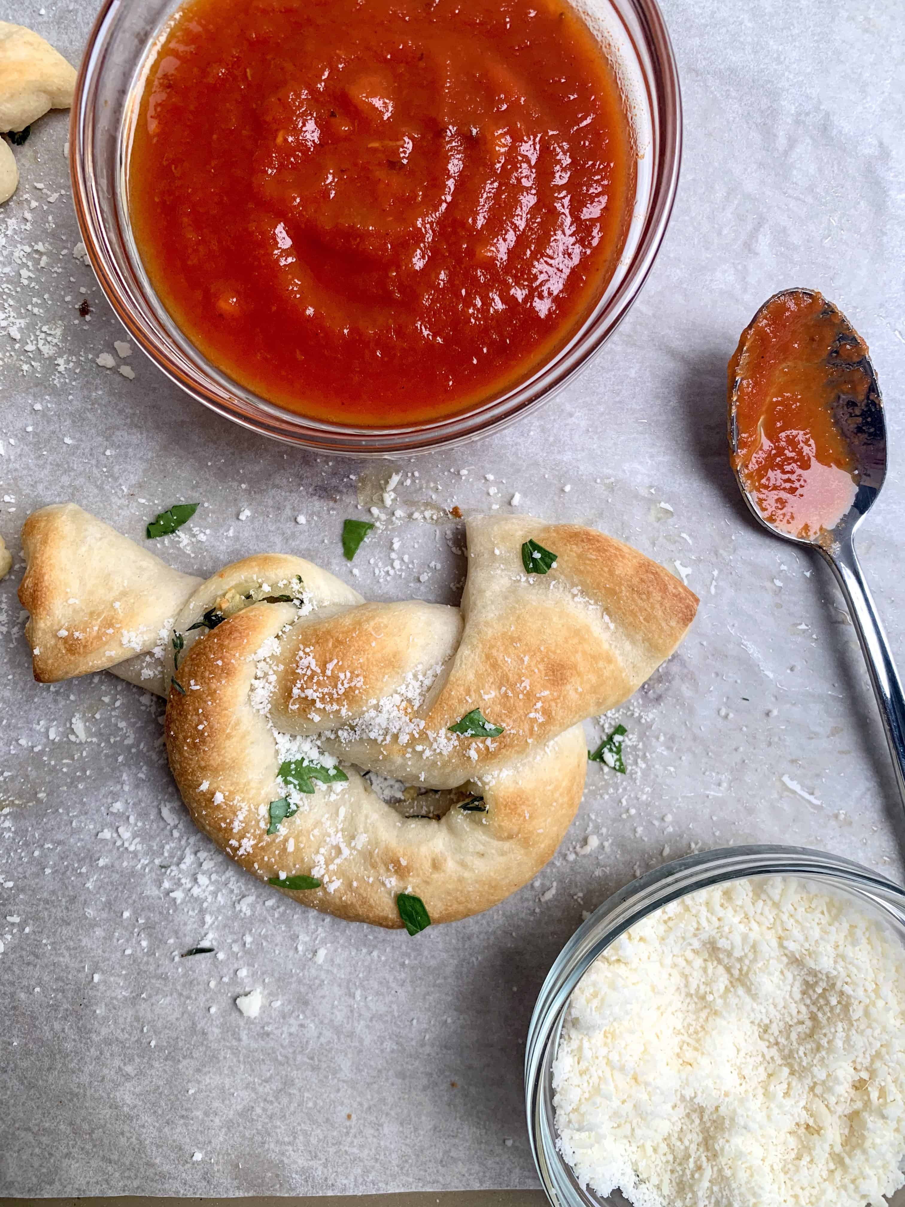 aerial up close picture of garlic knot with marinara and parmesan cheese in separate bowls with spoon