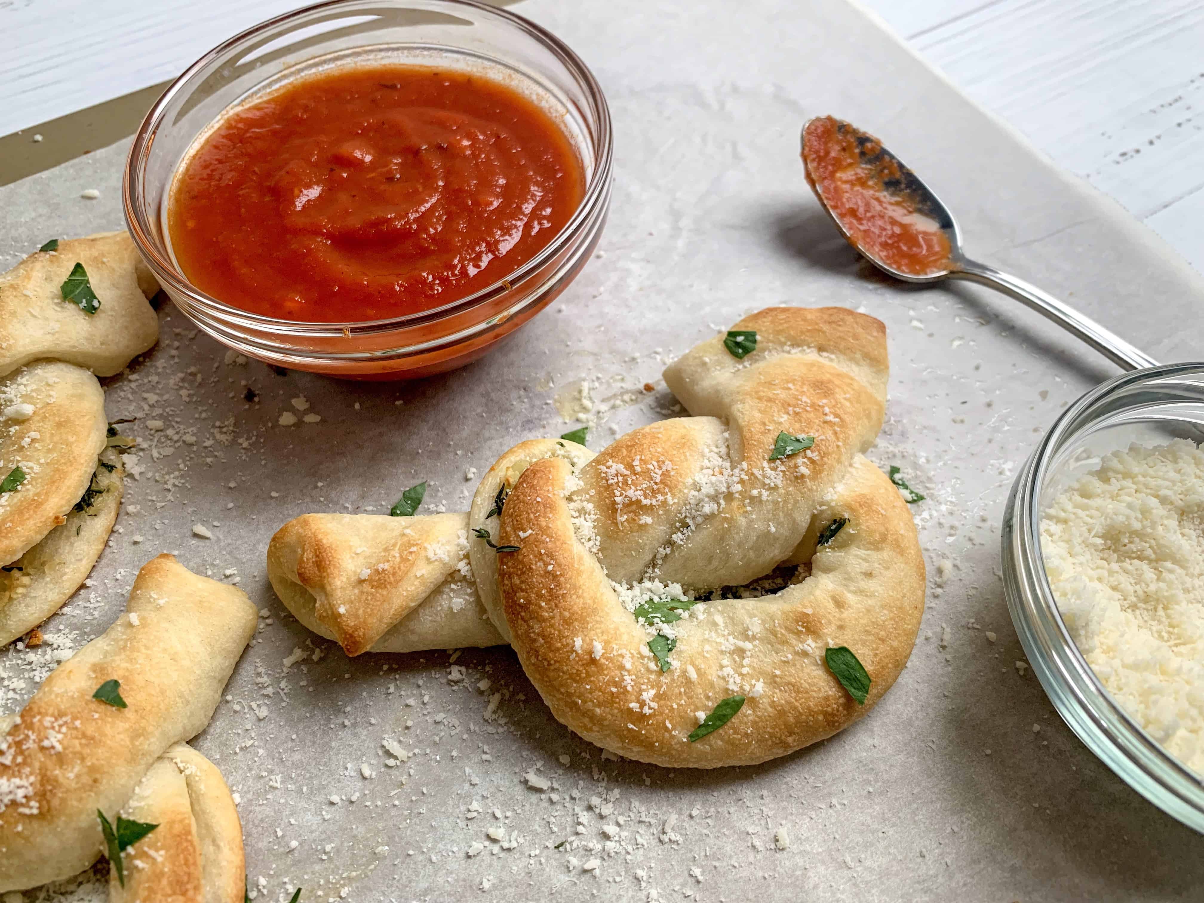 side view of garlic herb knots with bowl of marinara and parmesan cheese