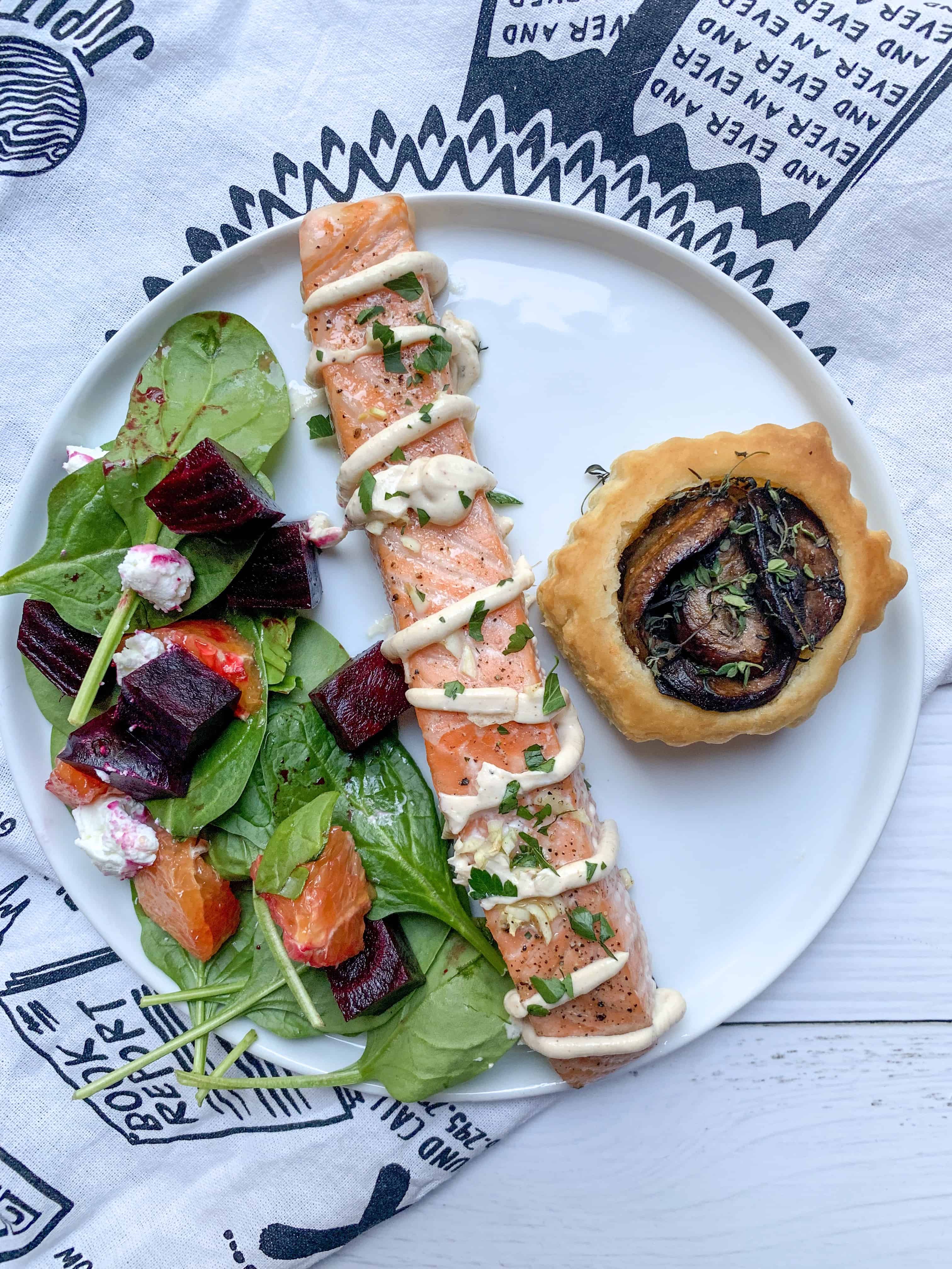 roasted salmon with yogurt tahini dressing, with a side salad and mushroom tart on a plate.