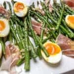 asparagus with prosciutto, jammy eggs, and a dijon vinaigrette on a white platter.