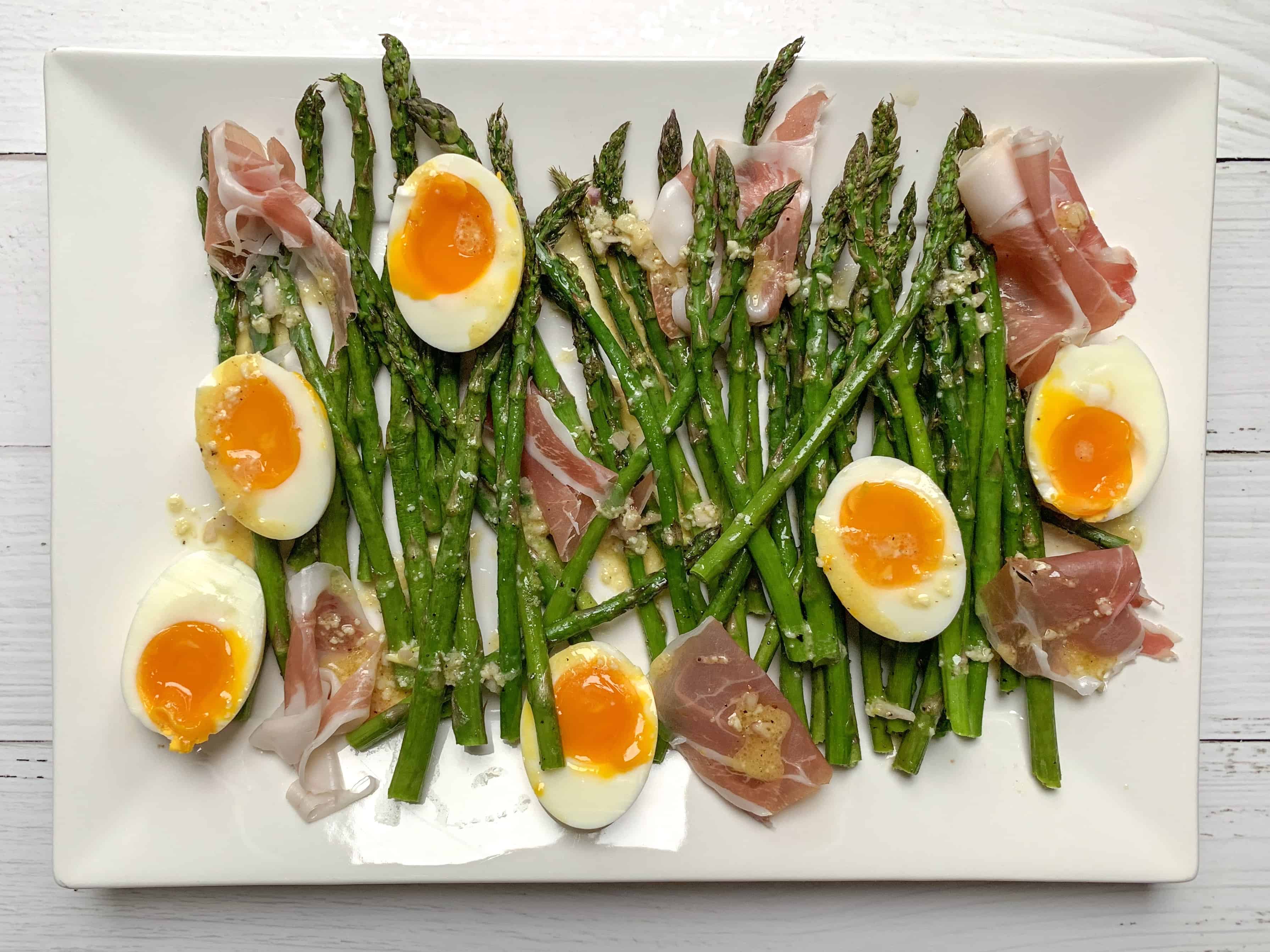 large white tray with the asparagus and jammy eggs tossed in dijon vinaigrette. 