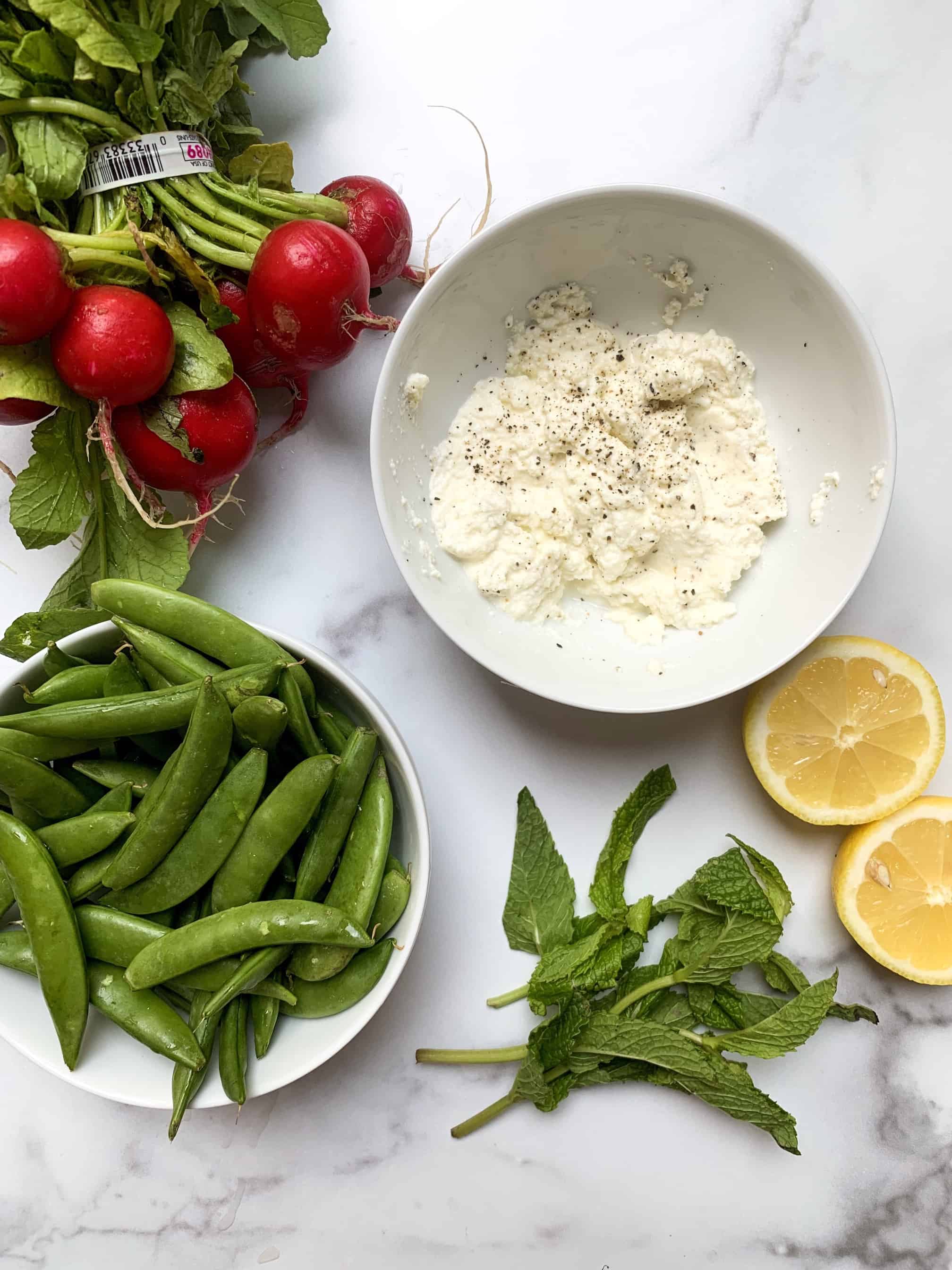 aerial shot of all ingredients needed for salad: ricotta, mint, lemon, sugar snap peas, and radishes.