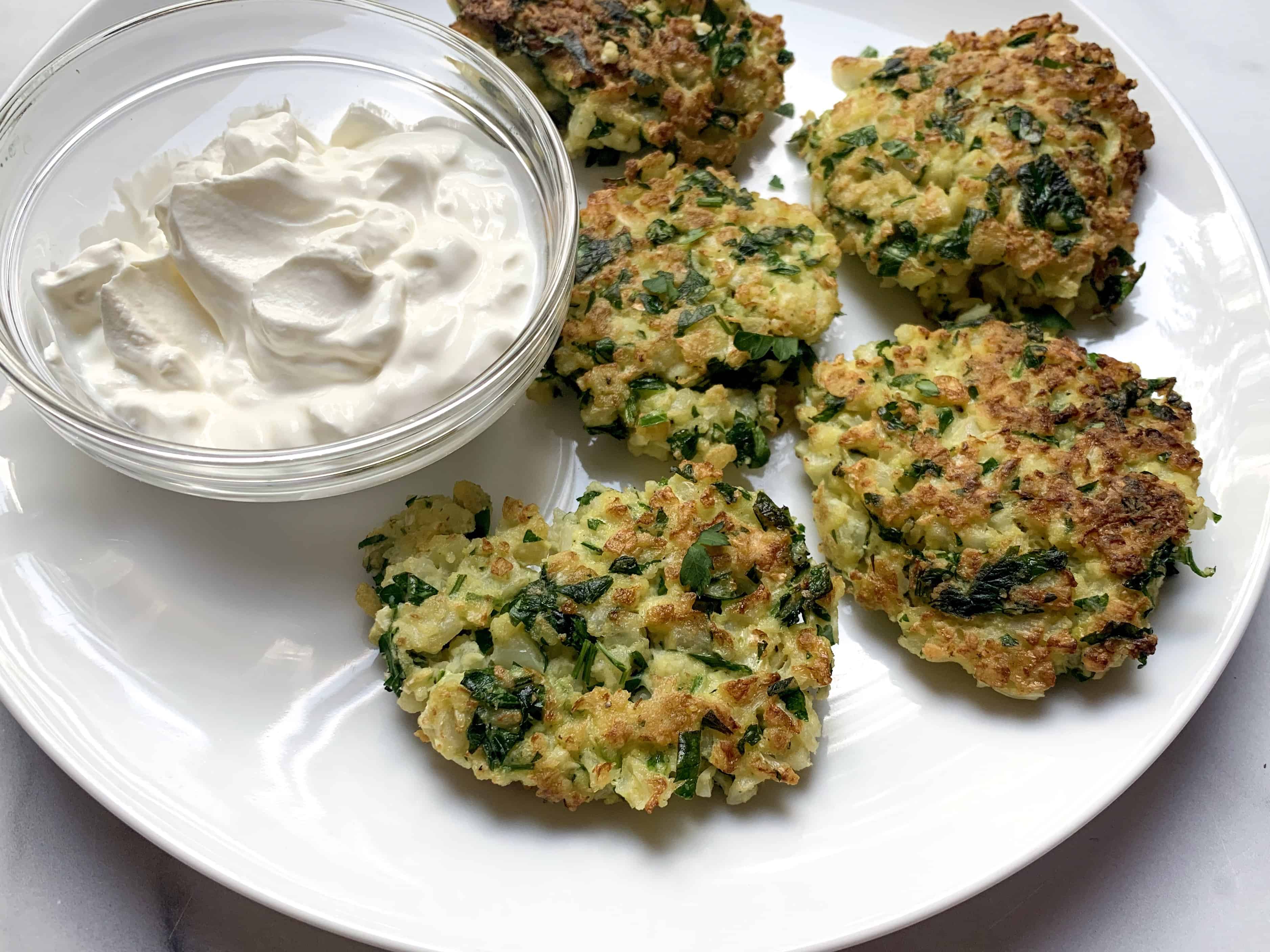 golden brown cauliflower fritters on plate with sour cream