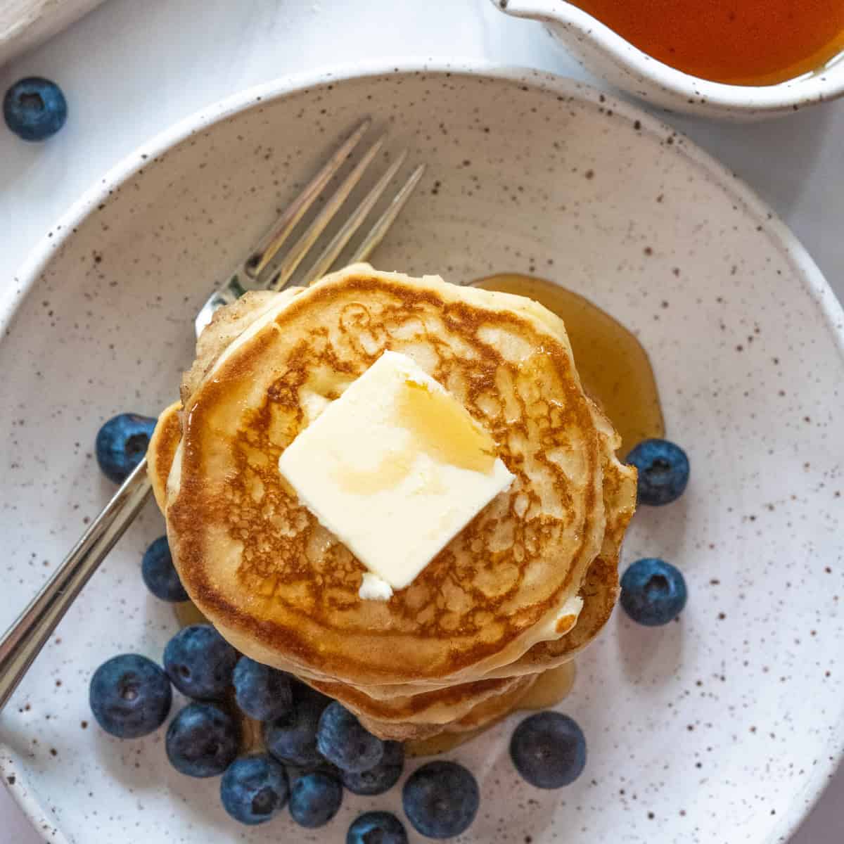 Top view of a stack of pancakes on a white plate with blueberries strewn around the bottom of the stack.
