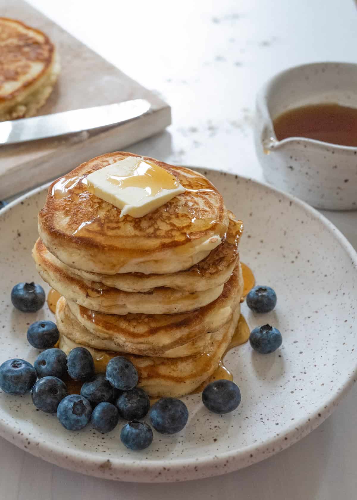 stack of pancakes with a slab of butter taken from 45 degree angle, showing maple syrup dripping from the top.
