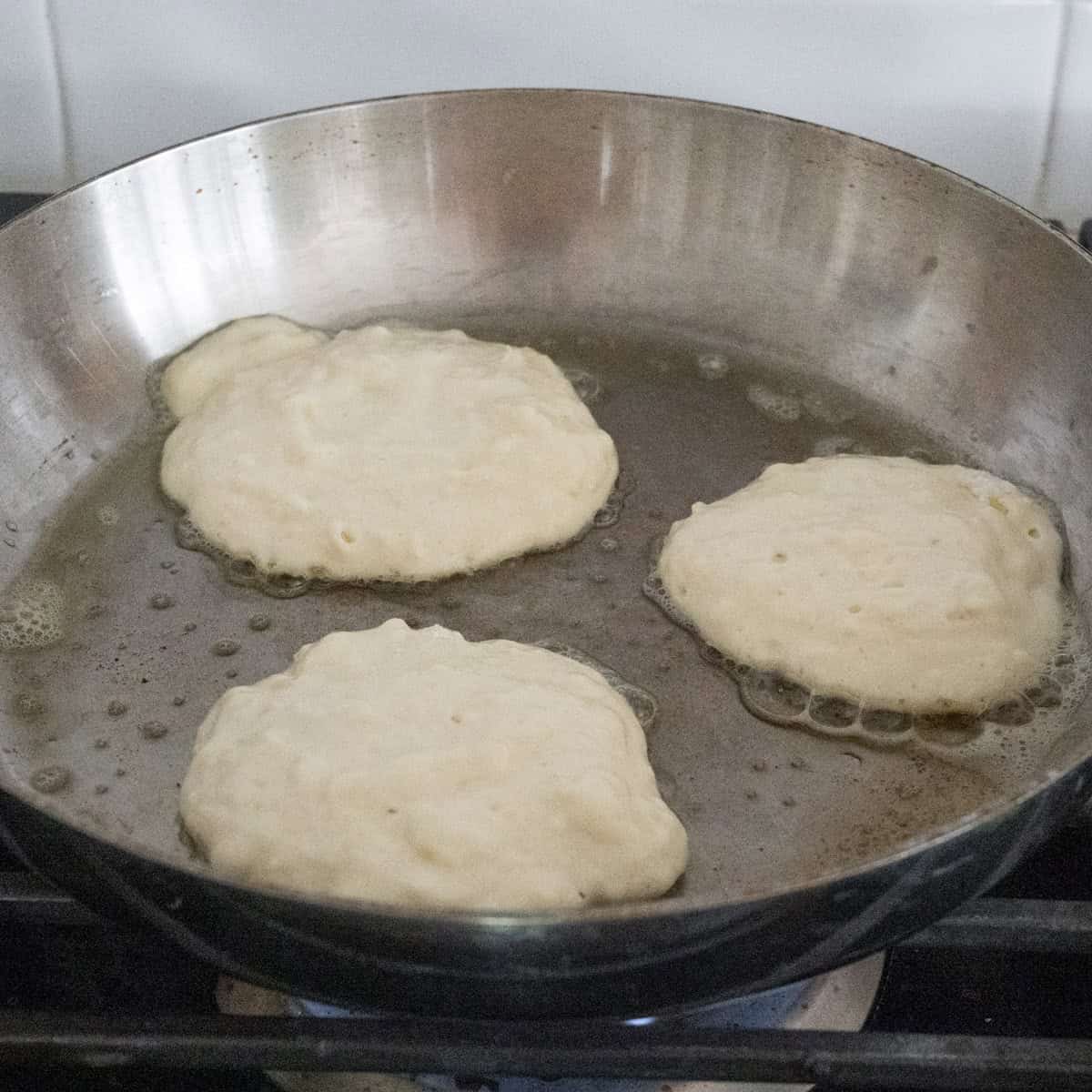 Step 4 of the directions showing pancakes cooking on a stainless steel pan.