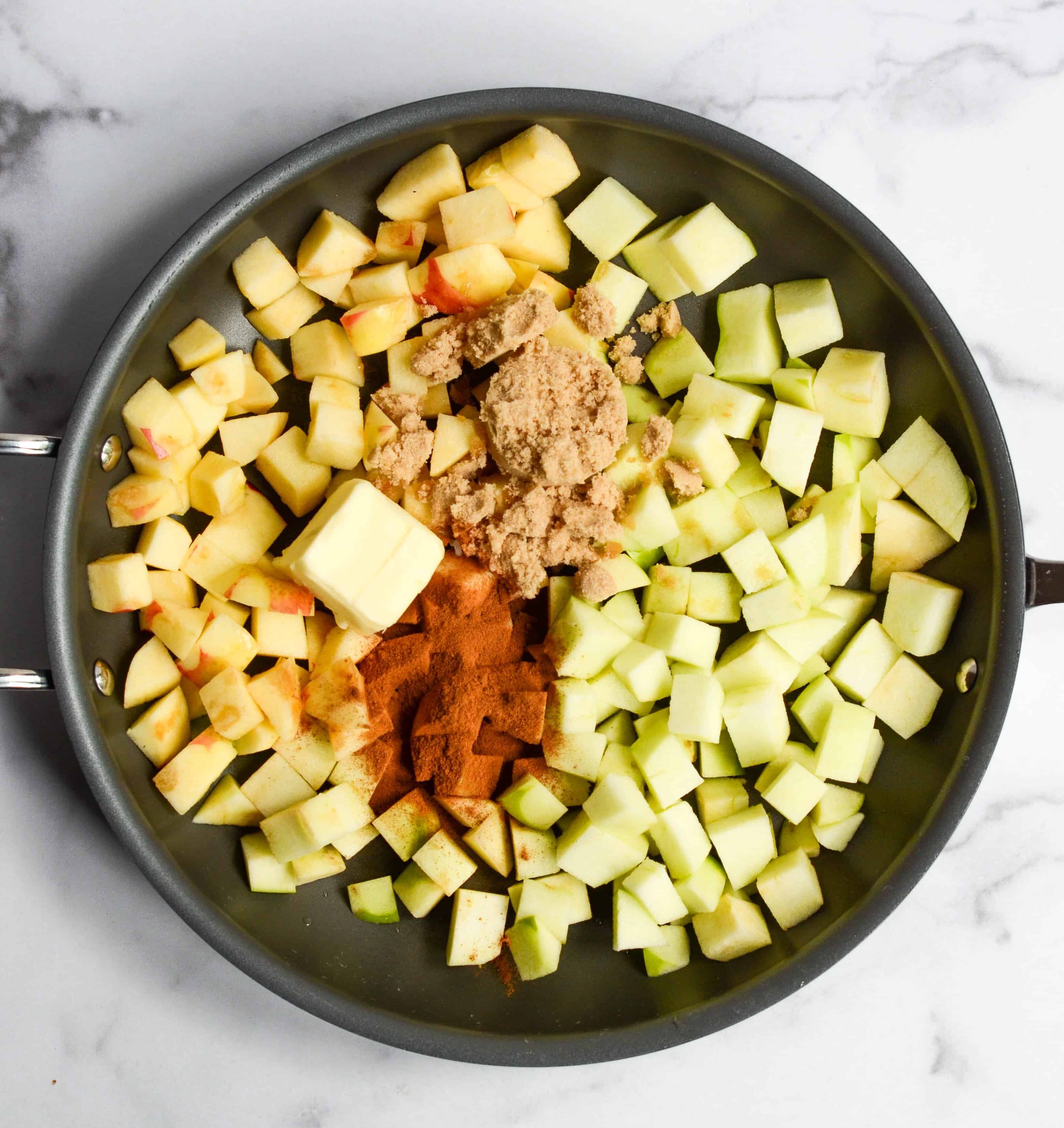 skillet with apples, brown sugar, cinnamon, and butter in it. 