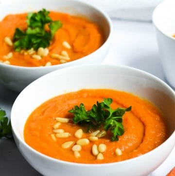 carrot ginger soup in a bowl with cilantro and pine nuts