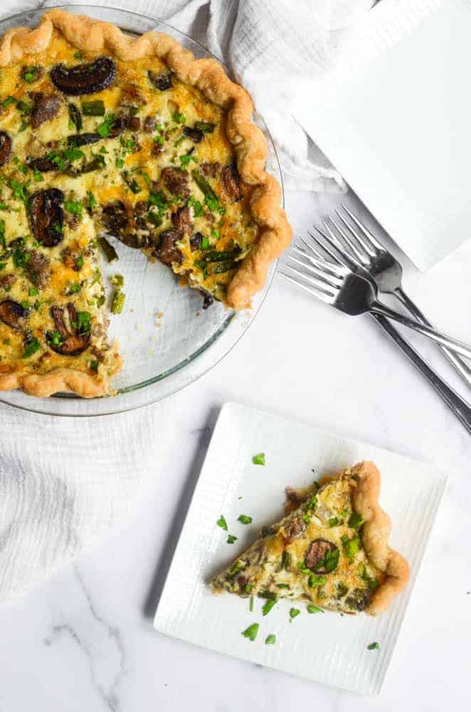 aerial view of both one slice of quiche and whole quiche with 3 forks next to quiche