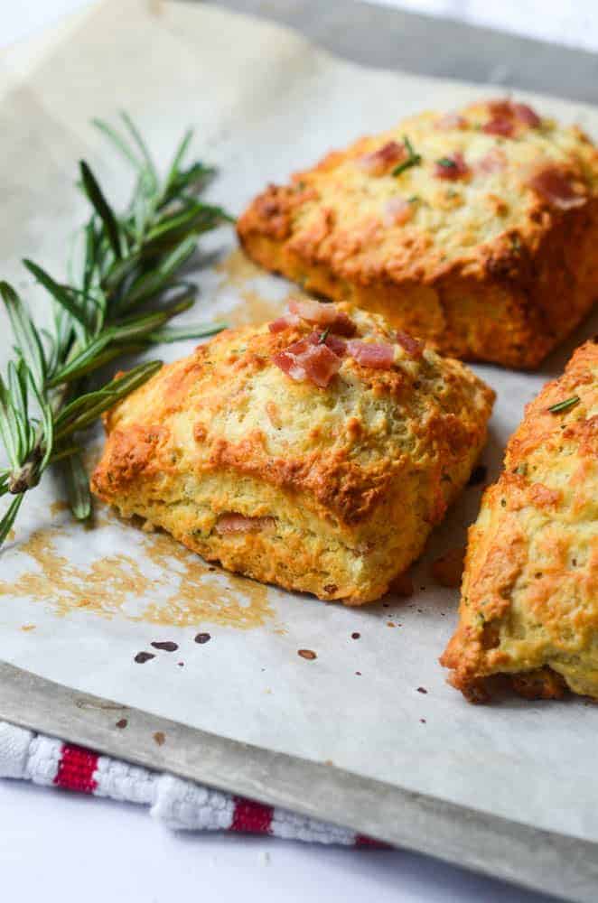 side angle shot of rosemary and bacon biscuits on baking sheet with sprig of rosemary