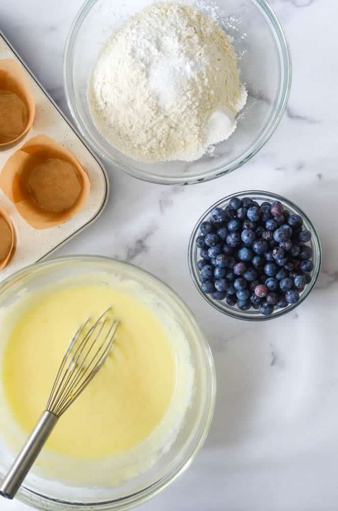 aerial view of bowl of wet ingredients with whisk, bowl of dry ingredients, and bowl of blueberries. 