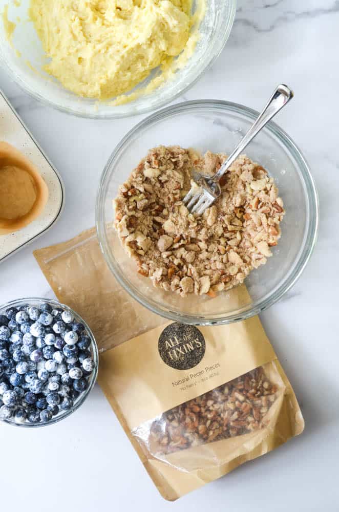 bag of pecans next to a bowl with the pecan streusel and blueberries covered in flour