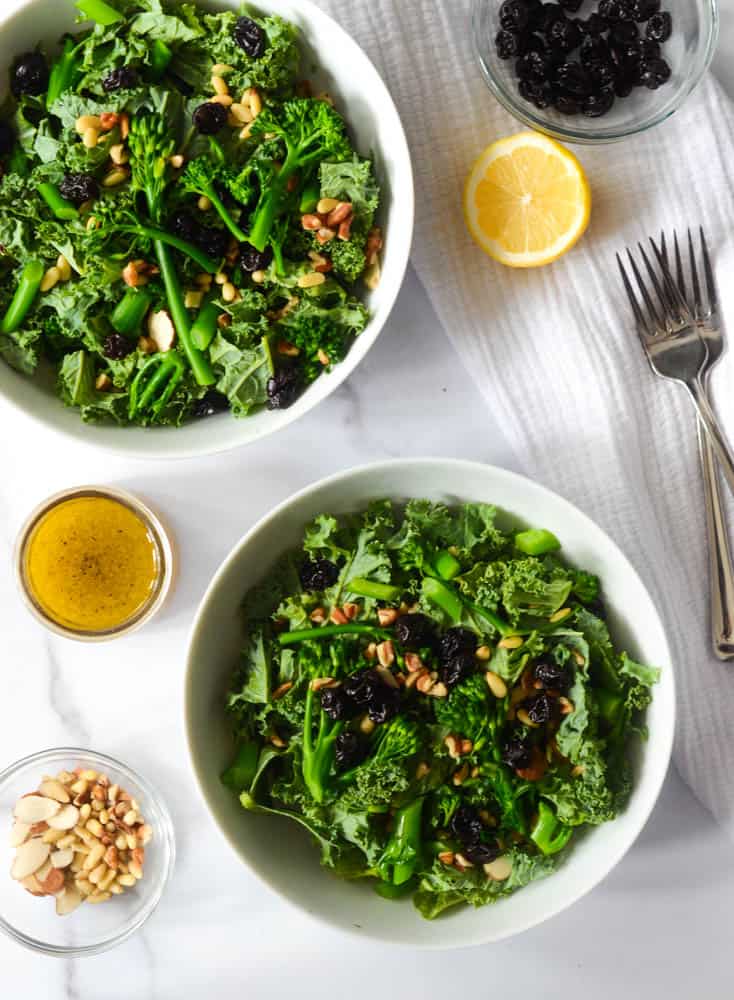 aerial view of two bowls with salad in them next to jar with vinaigrette, bowl of nuts, half a lemon, and sour cherries. 