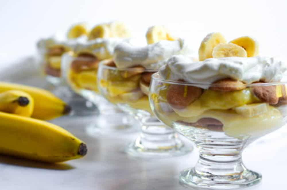one row of 4 nilla wafer pudding cups with bananas in the background