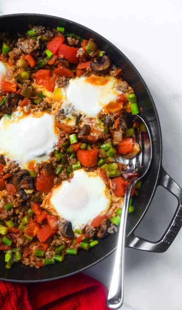 shakshuka in cast iron skillet with spoon under ingredients.