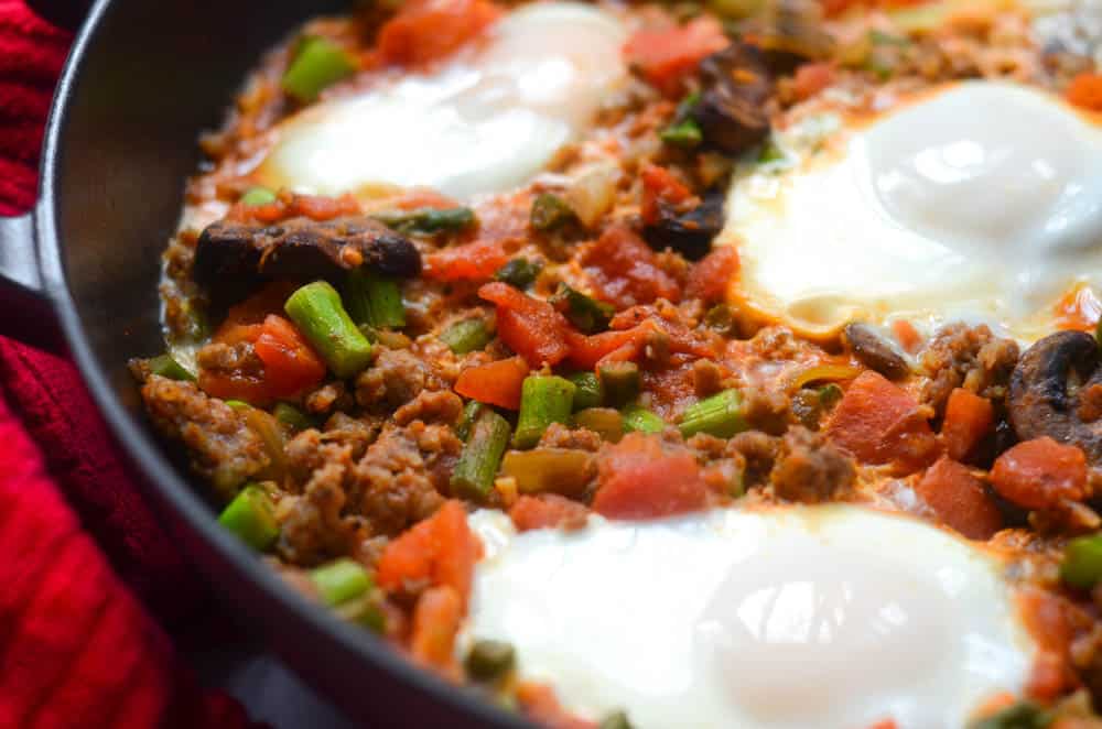 up close shot of vegetables and sausage in skillet with three poached eggs