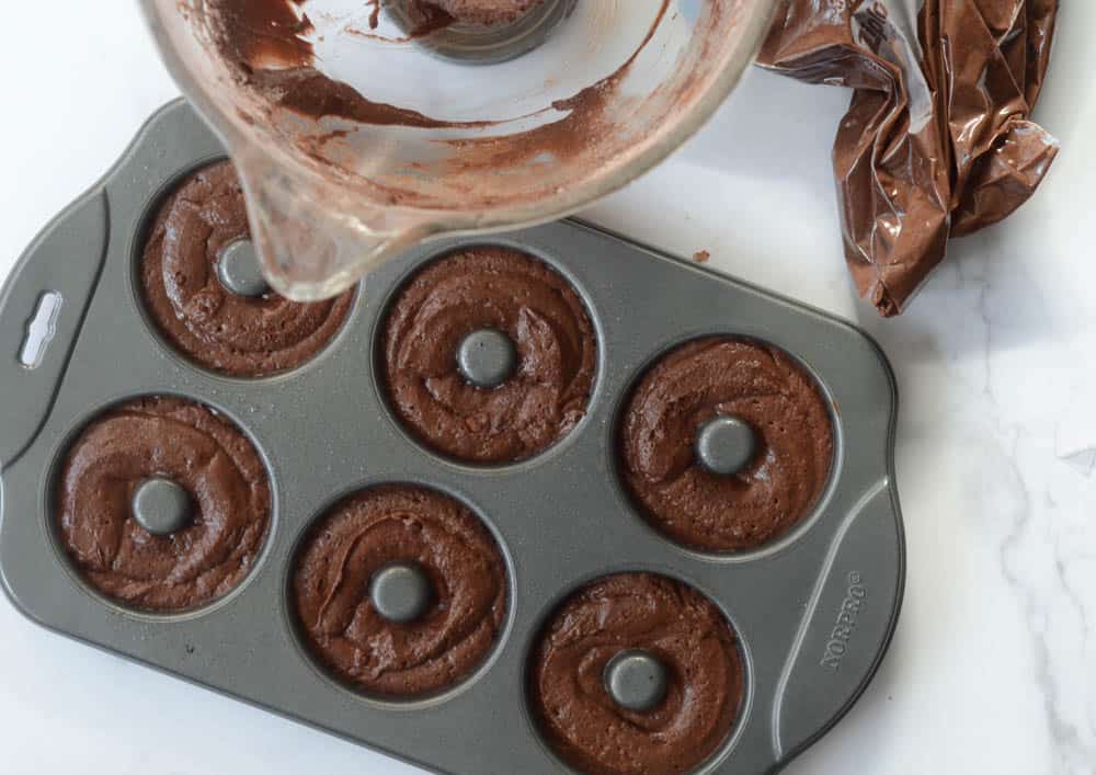 donut pan with chocolate donut batter in each cavity with bowl and plastic bag next to it.