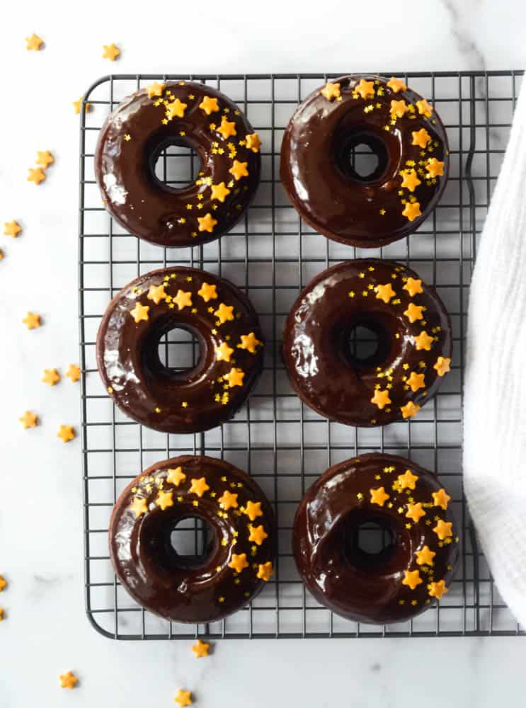 6 chocolate donuts on cooling rack with gold star sprinkles around them