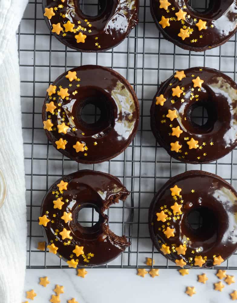 row of chocolate donuts on cooling rack with white kitchen towel