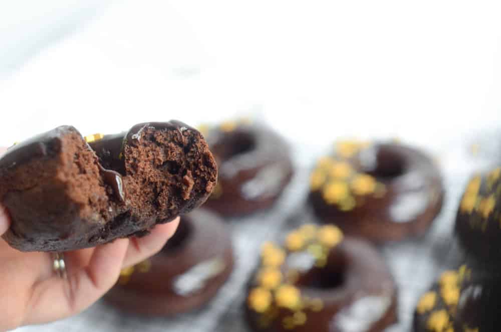 hand holding chocolate donut that's been bitten with other donuts in background