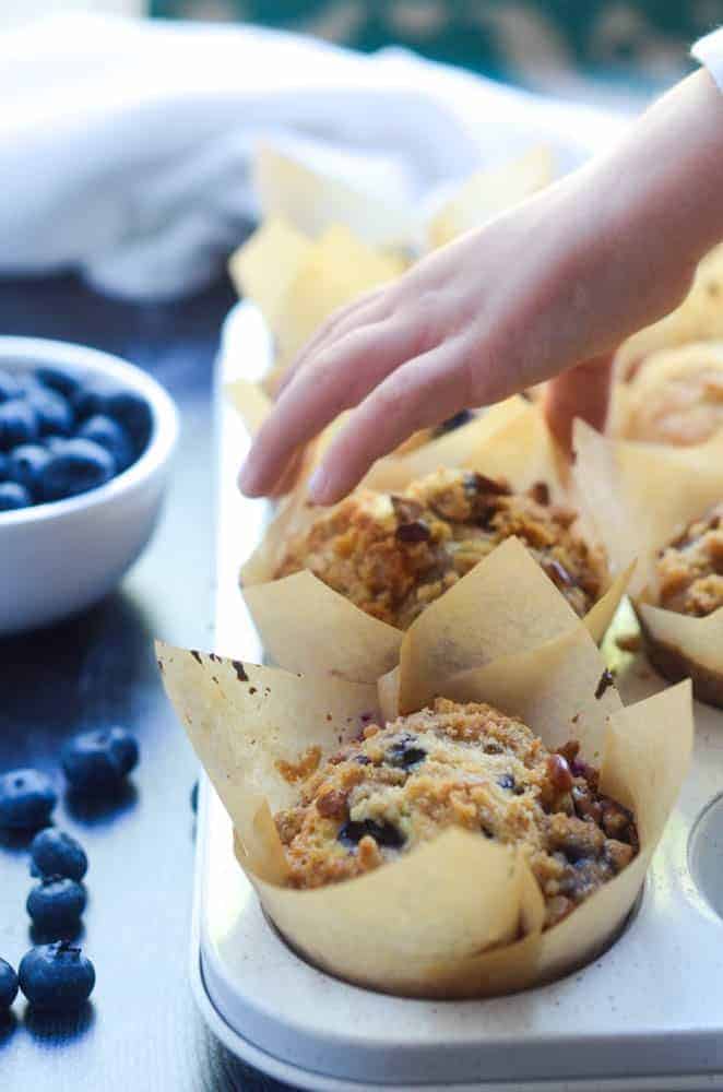 small child's hand about to grab a blueberry muffin with cup of blueberries in the background