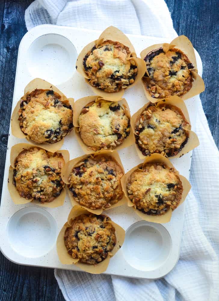 9 blueberry muffins sitting in white muffin tin on dark wood background