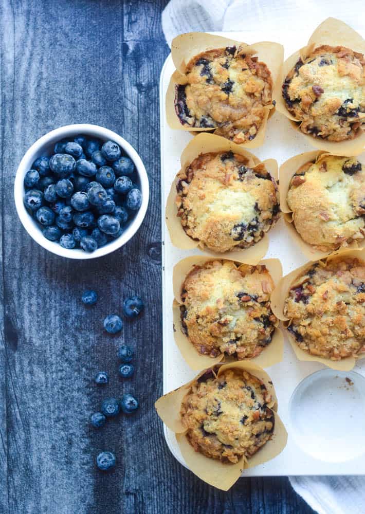 aerial view of blueberry muffins with bowl of blueberries next to it and some blueberries scattered on dark wood background