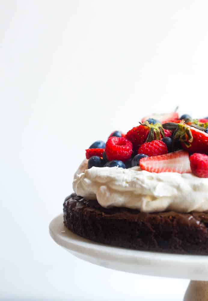 side view of brownie pizza cake with mixed berries on top of fluffy whipped cream on top of brownie
