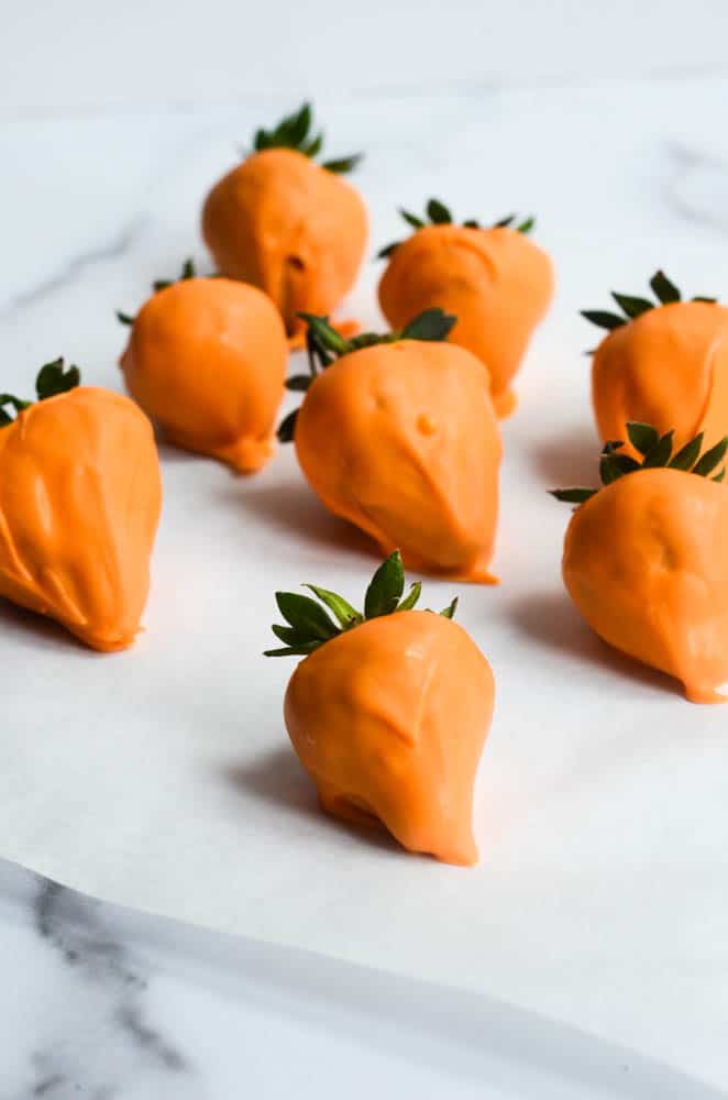 strawberries covered with orange candy melts on parchment paper