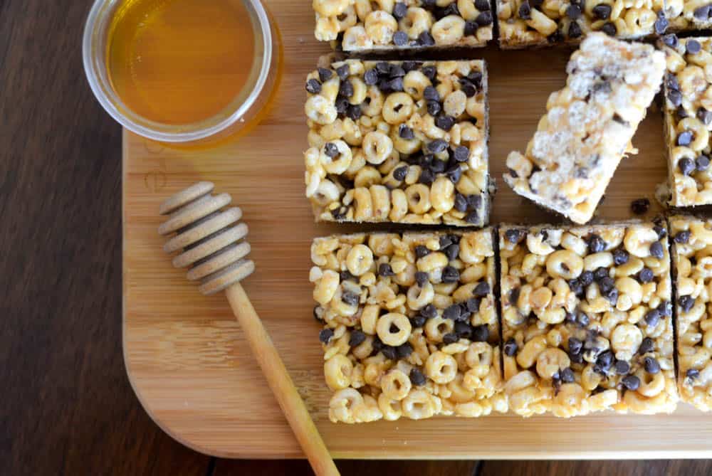 horizontal picture of homemade cereal bars on wooden cutting board with jar of honey and one bar turned on its side.