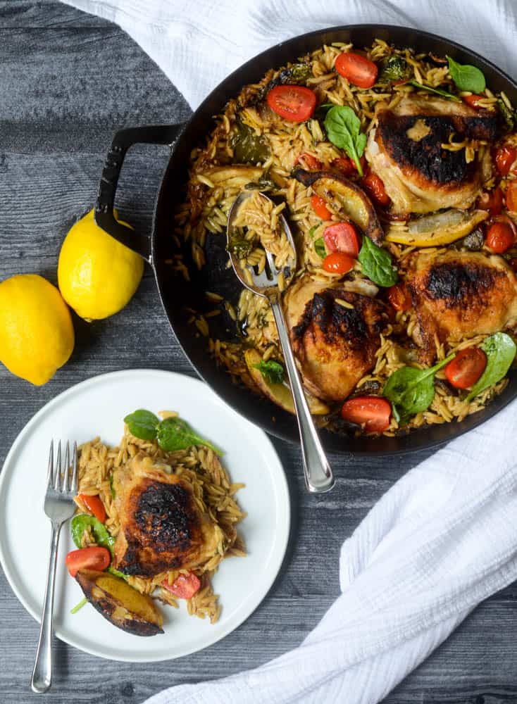 aerial view of skillet with lemon orzo chicken in it and plate where portion has been served. lemons in background.