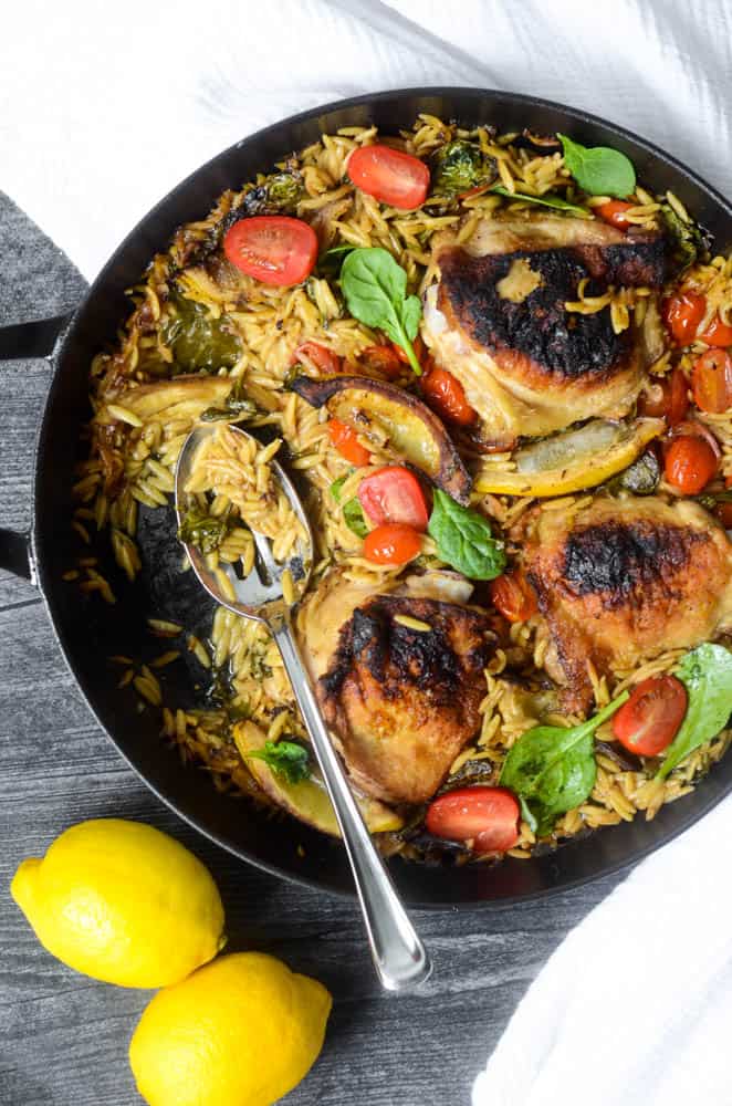 black skillet with lemon orzo chicken in it with spoon and portion taken out of pan