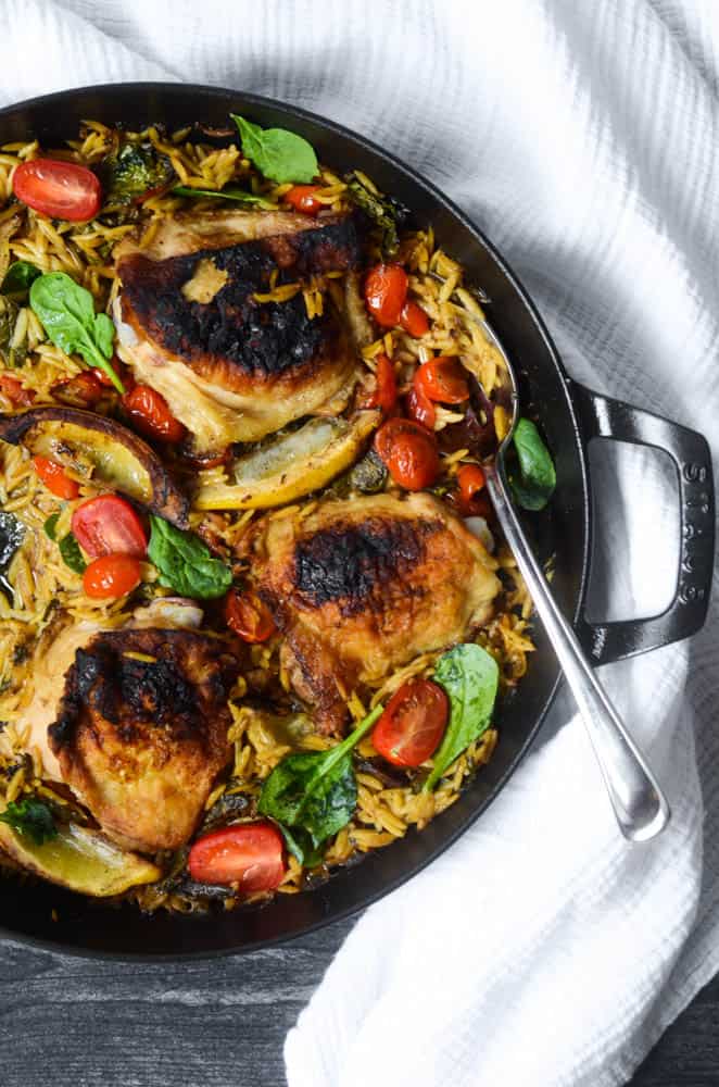 aerial view of black skillet with lemon chicken orzo with spoon in it.