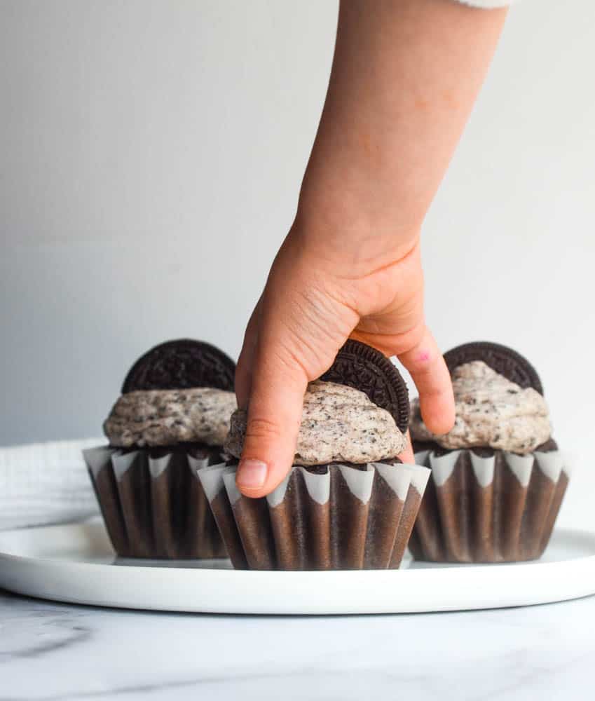 arm grabbing an chocolate cupcake with Oreo frosting 