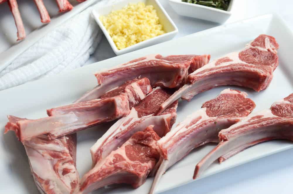 lamb chops sitting on white tray with garlic in the background