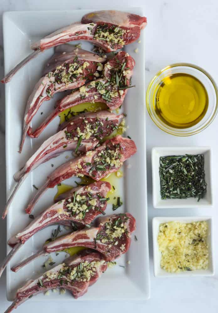 meat covered in olive oil, rosemary, and garlic with those three ingredients in small bowls