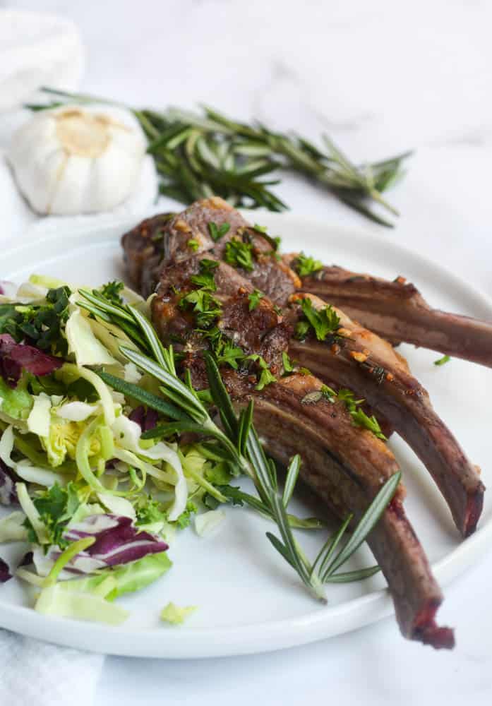 finished lamb on white plate with salad and sprig of rosemary