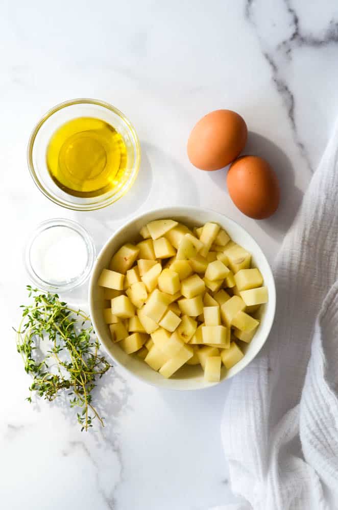 aerial shot of bowl of potatoes, thyme, salt, eggs, and olive oil 