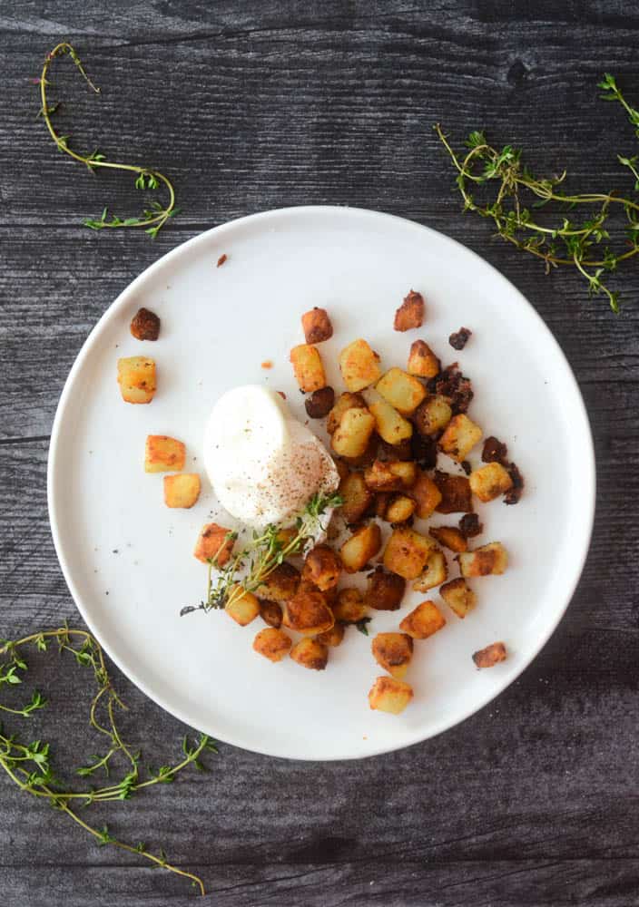 aerial shot of white plate with potatoes, poached egg, and sprig of time on black background