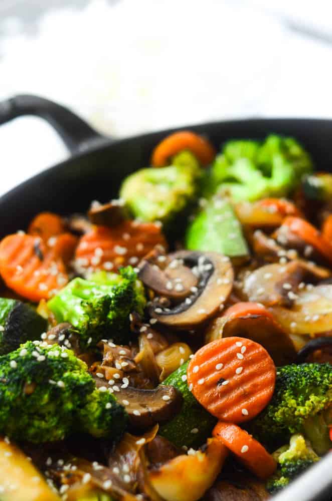 up close picture of vegetables sautéing in pan topped with sesame seeds 