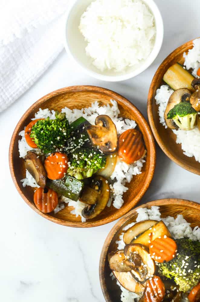 aerial view of three wooden plates with hibachi vegetables over steamed rice 