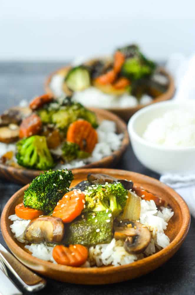 up close picture of one plate of hibachi vegetables on wooden plate with two other plates and white rice in background