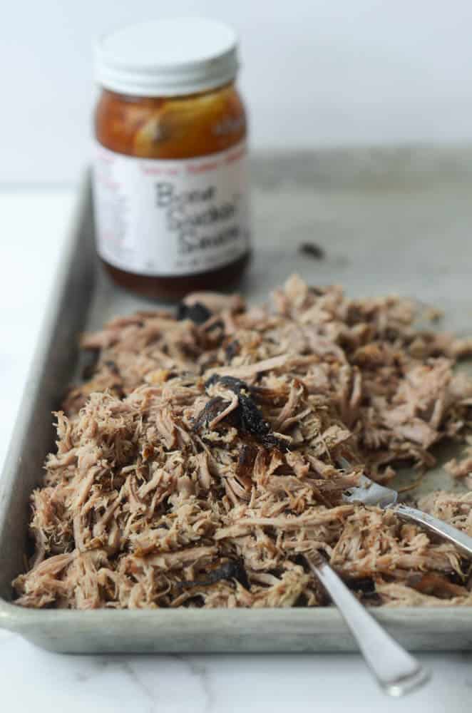 side view of dutch oven pulled pork on baking sheet with jar of barbecue sauce in the background