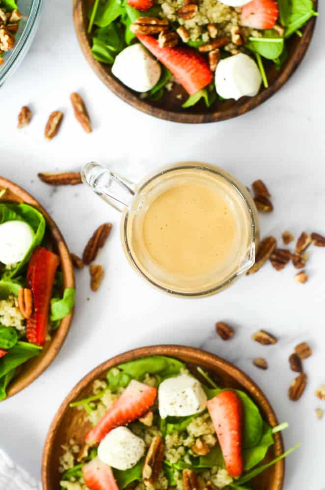 up close picture of creamy balsamic dressing in small pitcher with bowls of salad and pecans in background